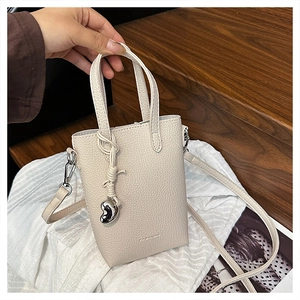 Détail du sac de téléphone en cuir crème avec texture litchi et pendentif en cœur