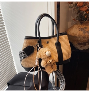 Détail du sac cabas en paille avec poignées en cuir noir et breloque ours en peluche