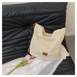 Detail of woven beige tote bag with brown leather straps on a black quilted background