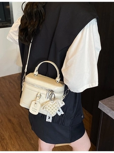 Minimalist cream vanity handbag with pearl heart charm shown from a side view