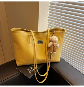 Detail of ginger yellow leather tote bag with plush bear charm on black leather bench
