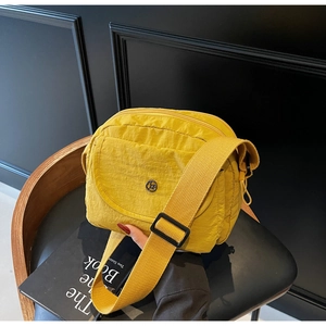 Detail der gelben Nylon-Umhängetasche mit Multi-Taschen und Metall-Logo auf einem Stuhl