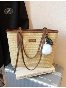 Bohemian straw tote bag with brown leather handles and decorative charm on a suitcase