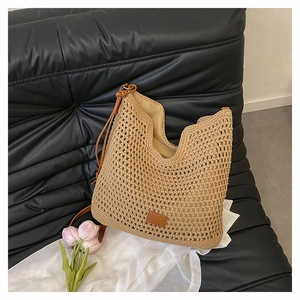 Detail of woven straw tote bag with brown leather strap on a black leather sofa