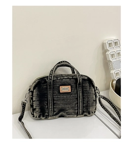 Détail du sac polochon en denim délavé avec écusson en cuir et deux poignées