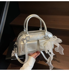 Detail of silver metallic Boston bag featuring twin front pockets and pearl bow charm