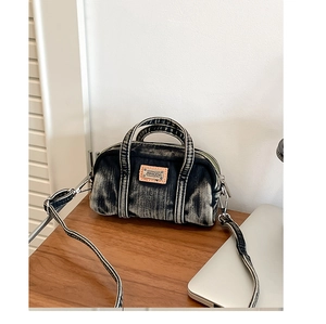Détail du sac Boston en denim délavé avec écusson logo en cuir et finitions argentées