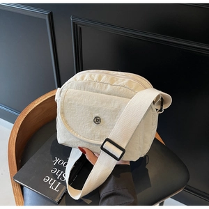 Detailansicht einer beige Nylon-Umhängetasche mit Doppelreißverschluss und Metalllogo