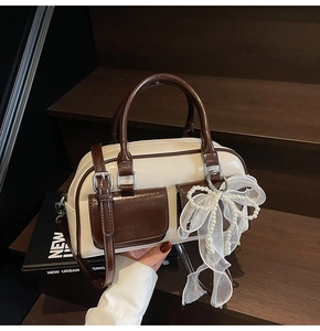 Close-up of cream Boston bag featuring brown leather pockets and a pearl bow charm