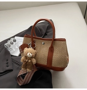 Détail d'un cabas en paille tressée avec garniture en cuir brun et breloque ours mignon