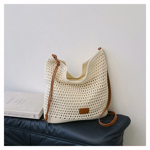 Detail of hand-woven cream crochet shoulder bag with brown leather strap and logo patch