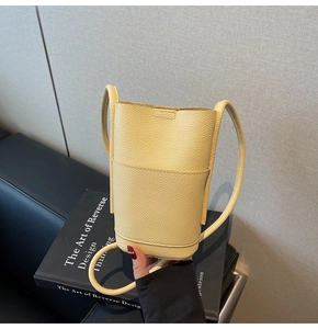 Detail of yellow pebbled leather bucket bag featuring front pocket and thin cord strap