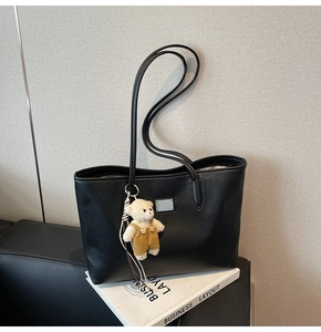 Detail of black tote bag with lychee texture and cute bear pendant on business book
