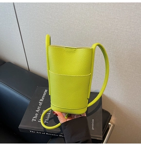 Detail of lime green pebble leather mini crossbody phone bag on a black leather sofa