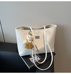 Close-up of white lychee leather tote bag with a cute bear charm and metal nameplate