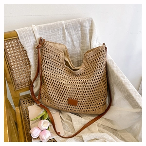 Close-up of beige woven hobo bag on a rattan chair with brown leather strap detail