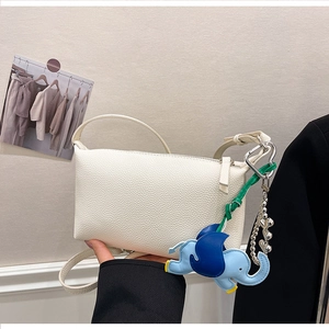 Dettaglio borsa a bauletto in pelle bianca con ciondolo a elefante blu e catena a sfere