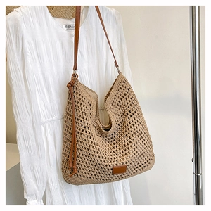 Detail of woven straw tote bag with brown leather shoulder straps and tassel accents