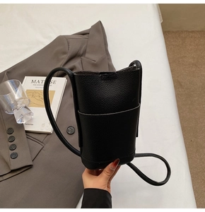 Detail of black litchi grain leather bucket phone bag held against a grey blazer