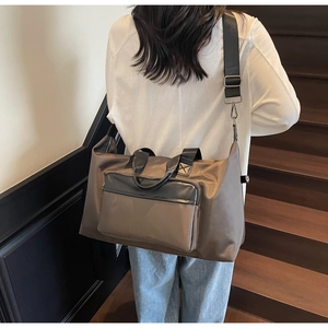 Deep brown nylon travel bag with front zip pocket and adjustable strap on a wood stairs