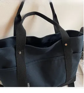 Close-up of large black canvas tote bag showing durable fabric and front pocket detail