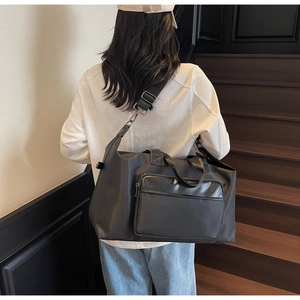 Large black travel bag with adjustable strap worn as crossbody in a modern urban setting