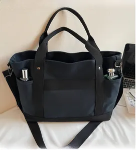 Detail of a black canvas tote bag featuring functional front pockets and sturdy handles