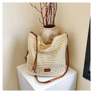 Detailed view of cream woven shoulder bag with brown leather strap on a geometric base