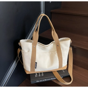 Detail of canvas tote bag showing beige fabric, khaki straps, and side brand label