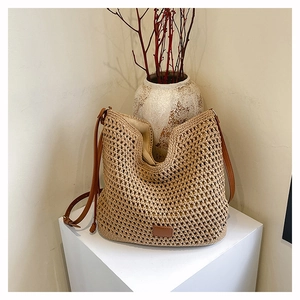 Detailed view of beige woven tote bag with brown leather straps on a geometric stand