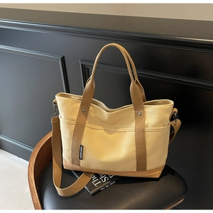 Detail of canvas tote bag with top handles, long strap and woven label on a chair