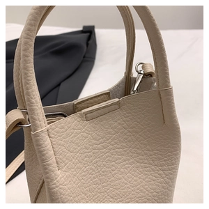 Detail view of cream pebbled leather bucket bag with silver metal buckle and fine stitching