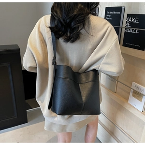 Close-up of black lychee grain leather bucket bag shown on model with beige knitwear