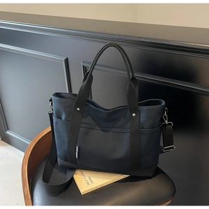 Detailed view of black canvas tote bag with detachable shoulder strap and side pocket