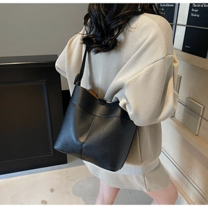 Side view of black lychee grain leather bucket bag worn by model in a minimalist setting