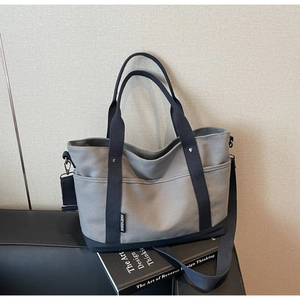 Detail of grey and navy canvas tote bag with adjustable shoulder strap on leather bench