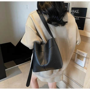 Close-up of black lychee grain leather bucket bag with wide shoulder strap on model