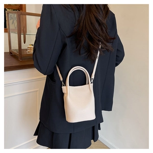 Close-up of beige lychee texture bucket bag worn by model in a cozy cafe setting