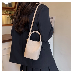 Chic cream bucket bag with litchi texture shown on a model in a minimalist setting
