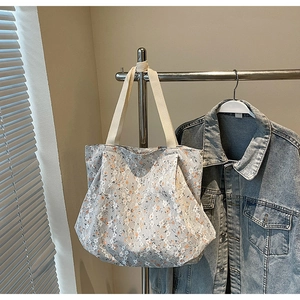 Floral lace tote bag detail in light grey with orange flowers hanging on a metal rack
