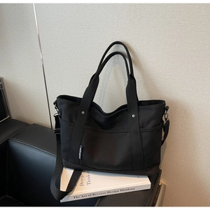 Detail of black canvas tote showing reinforced silver rivets and adjustable shoulder strap