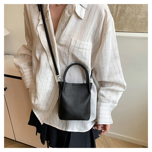 Detail of a black pebbled leather bucket bag with an adjustable strap and curved handle