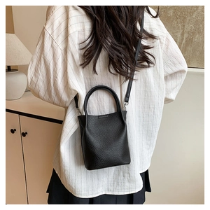 Close-up of black lychee texture leather bucket bag worn with a white striped shirt