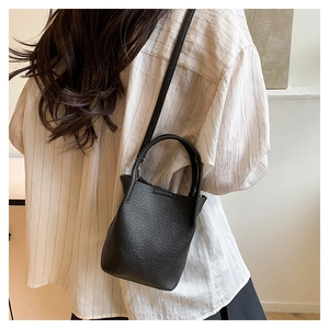 Close-up of black litchi grain leather bucket bag worn as a crossbody on model
