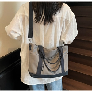 Detailed view of grey canvas tote bag with navy blue handles and wide black nylon strap