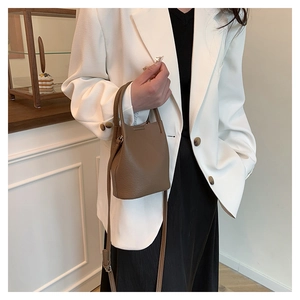 Detailed view of a brown lychee pattern leather bucket bag worn by a model in a suit