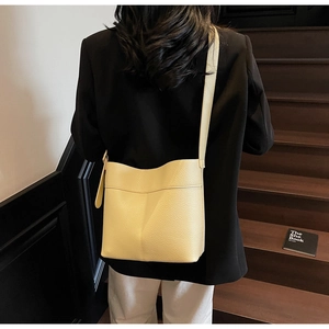 Detailed view of cream yellow bucket bag with lychee grain texture worn over the shoulder