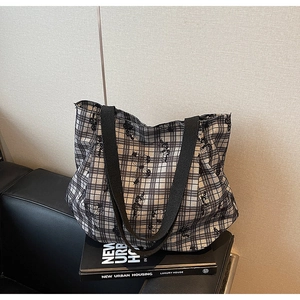 Close-up of black and white checkered canvas tote bag with wide straps on urban book