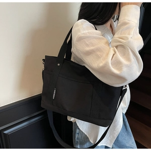Detail of black canvas tote bag showing handle, adjustable strap, and side brand label
