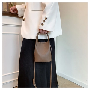 Close-up of mocha bucket bag with lychee texture held by model in white blazer